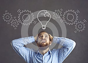 Stressed businessman looking at a cracked idea light bulb with a broken chain of gears