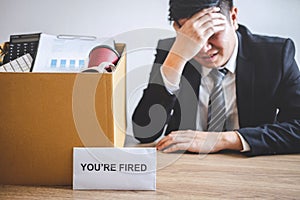Stressed businessman receive fired letter from company and packing belongings and files into brown cardboard box, changing and