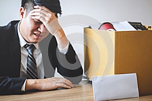 Stressed businessman receive fired letter from company and packing belongings and files into brown cardboard box, changing and