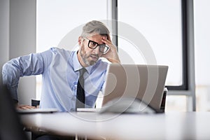 Stressed businessman sitting at desk and working on laptop at the office