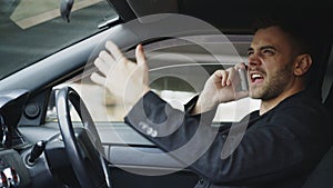 Stressed businessman swearing and talking phone while sitting inside car outdoors