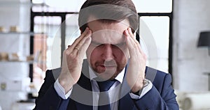 Stressed businessman wearing suit massaging temples suffering from migraine