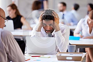 Stressed Businessman Working On Laptop In Busy Office