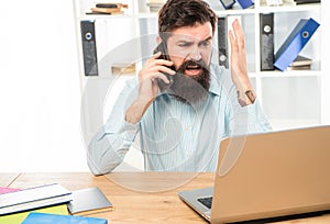 Stressed businessman yelling on mobile phone working on laptop in office, stress
