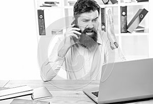 Stressed businessman yelling on mobile phone working on laptop in office, stress