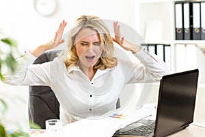 Stressed businesswoman screaming loudly at laptop