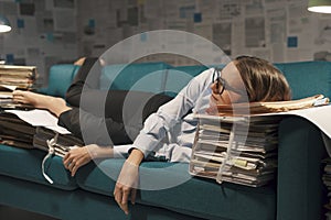 Stressed businesswoman sleeping on a couch with lots of paperwork