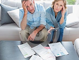 Stressed couple sitting on their couch paying their bills