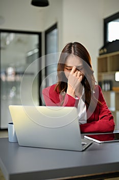 Stressed and depressed Asian businesswoman sits at her office desk, suffering from eyes strain