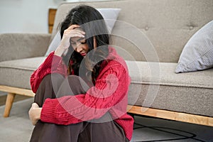 Stressed and depressed Asian woman sits in living room, suffering from her life issues