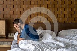 Stressed, depressed or grieving man sitting on bed covering face with hands and crying. Worried and frustrated male