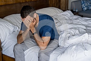 Stressed, depressed or grieving man sitting on bed covering face with hands and crying. Worried and frustrated male