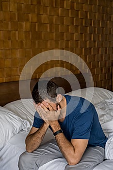 Stressed, depressed or grieving man sitting on bed covering face with hands and crying. Worried and frustrated male