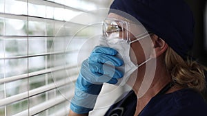 Stressed Doctor or Nurse On Break Opens Blinds At Window Wearing Face Mask and Protective Glasses