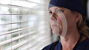 Stressed Doctor or Nurse On Break At Window Wearing Stethoscope and Scrubs