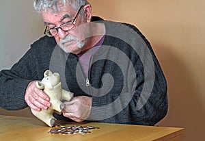 Stressed elderly man emptying piggy bank.