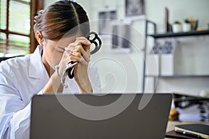 Stressed and exhausted Asian female doctor at her office desk, feeling tired