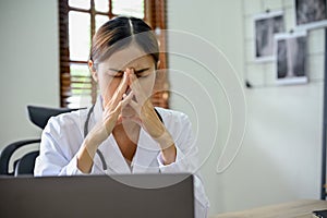 Stressed and exhausted Asian female doctor sitting at her office desk