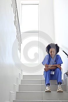 Stressed Female Doctor Or Nurse Wearing Scrubs Sitting On Stairs In Hospital 