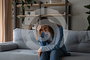 Stressed female sit on couch alone look down having problem