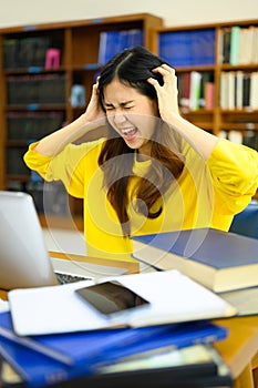 Stressed female student sitting in front of the laptop, having serious computer problem or feeling tired of studying for
