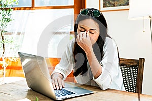 Stressed female working on laptop while touching her forehead. Tired young woman feel pain eye strain from computer work. Over