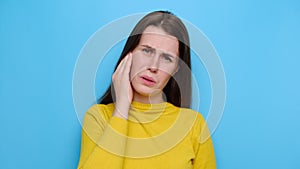 Stressed frowning young woman plugging ear, feeling painful discomfort, avoids bad sound, wears yellow sweater