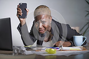 Stressed and frustrated afro American black woman working overwhelmed and upset at office laptop computer holding mobile phone in