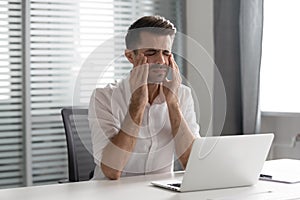 Stressed frustrated businessman suffer from strong headache attack at workplace