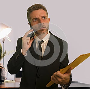 Stressed and frustrated businessman talking on mobile phone holding paperwork reports upset and worried in business problems and