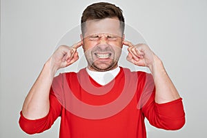 Stressed frustrated man plugging his ears with fingers and keeping eyes closed