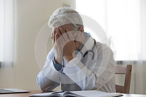 Stressed frustrated mature doctor covering face with hands