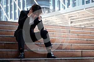 Stressed frustrated young Asian businessman sitting on stairway outside office in downtown city. man put his head in his hand