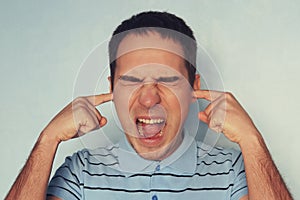 Stressed frustrated young man plugging his ears with fingers and keeping eyes closed while having headache, can`t stand terrible