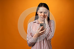 Stressed frustrated young woman holding smartphone, recieved bad news, yellow background