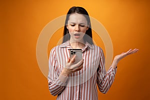 Stressed frustrated young woman holding smartphone, recieved bad news, yellow background