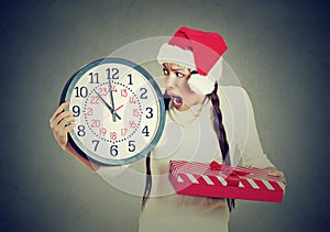 Stressed in a hurry woman wearing santa claus hat holding clock gift box