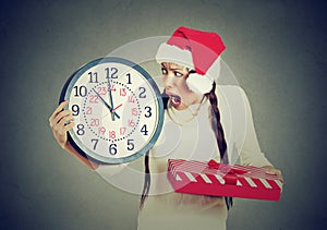 Stressed in a hurry woman wearing santa claus hat holding clock gift box photo