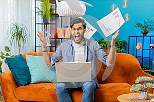 Stressed Indian man looking at unpaid bank debt loan, doing paperwork planning budget throws bills