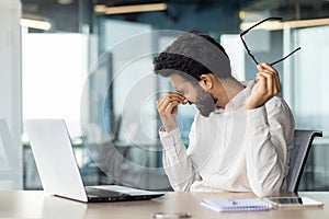 Exhausted indian businessman feeling stressed at work while sitting at his office desk photo