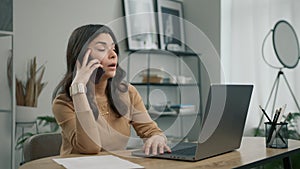 Stressed latin woman works on desktop computer and speaking using smartphone 4K