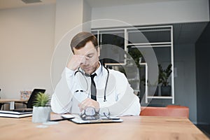 Stressed male doctor. Mid adult male doctor working long hours. Overworked doctor in his office. Not even doctors are