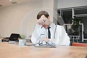 Stressed male doctor. Mid adult male doctor working long hours. Overworked doctor in his office. Not even doctors are