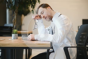 Stressed male doctor sat at his desk. Mid adult male doctor working long hours. Overworked doctor in his office. Not