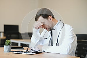 Stressed male doctor sat at his desk. Mid adult male doctor working long hours. Overworked doctor in his office. Not