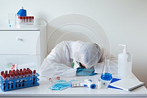 Stressed male doctor sitting tired at his desk. Mid adult male doctor working long hours in protective clothes. Covid-19