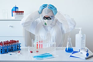 Stressed male doctor sitting tired at his desk. Mid adult male doctor working long hours in protective clothes. Covid-19