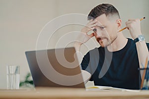 Stressed male office worker looking at laptop with worried face expression