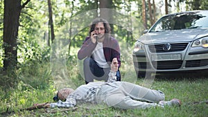 Stressed man calling ambulance checking pulse of knocked down woman outdoors. Portrait of young Caucasian driver and