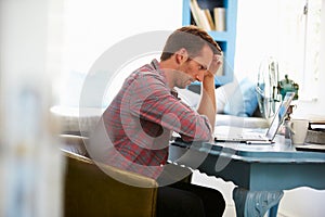 Stressed Man At Desk In Home Office With Laptop